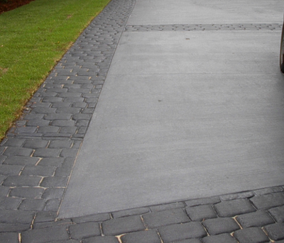 Worn and weathered stamped edging with plain gray concrete driveway.