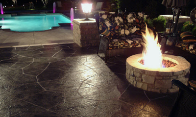 Dark brown stone stamped concrete patio adjacent to a built in pool.